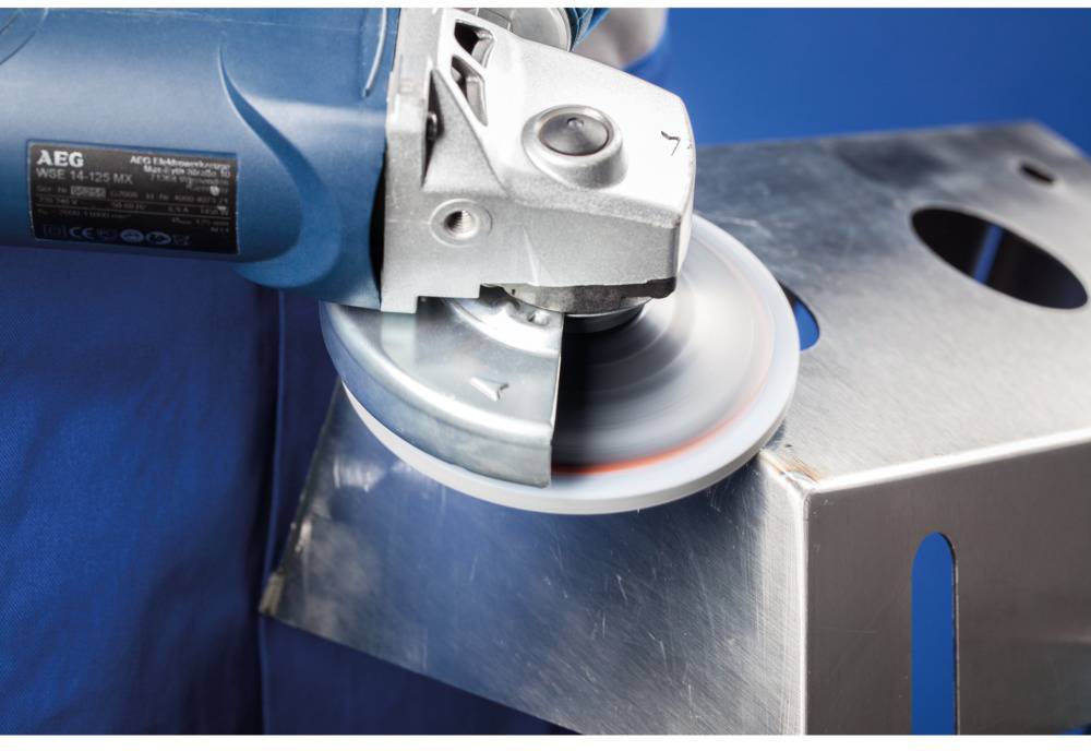 A person is using an angle grinder to grind a metal surface. The sparks indicate active processing.<br><br>Translation to British English:<br>A person is using an angle grinder to grind a metal surface. The sparks show active machining.