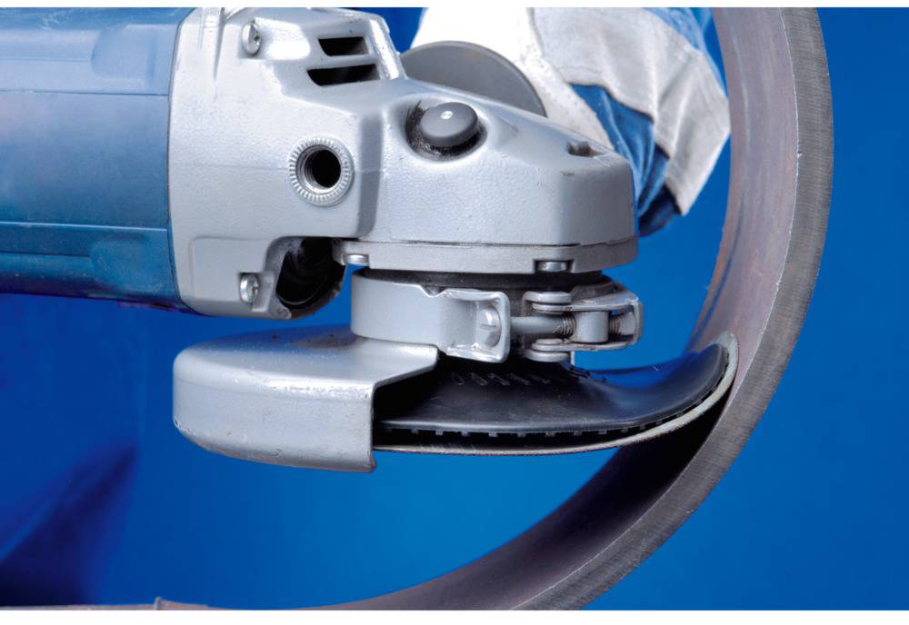 An angle grinder with a disc is cutting through metal. A person wearing safety clothing is holding the tool firmly.