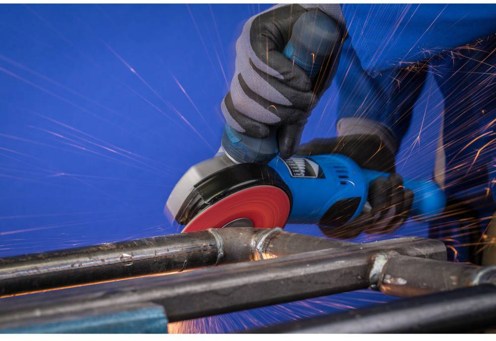 A person is grinding metal pipes with an angle grinder, sparks are flying, focusing on the work process and safety gloves.