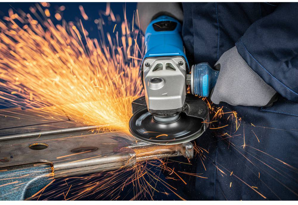 A person is using an angle grinder, sparks flying. Safety clothing is being worn, metal is being cut.