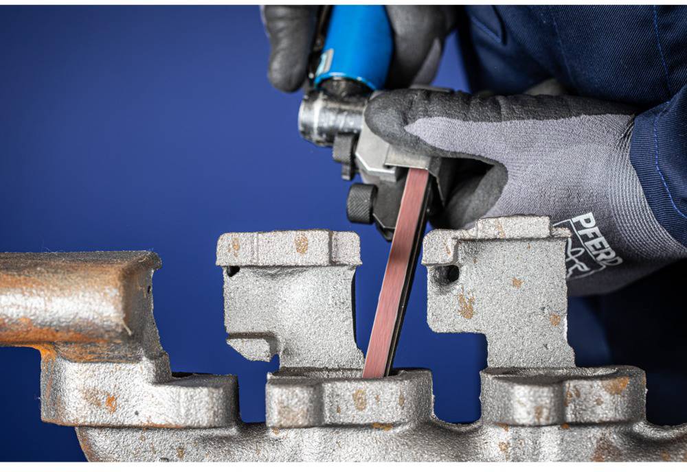 A person is grinding a metal part with a blue belt sander in a vice. Typical workshop environment.