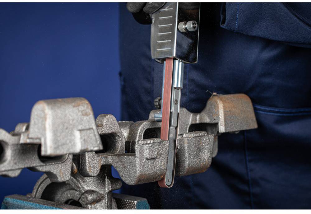 A person is grinding a metal part with a rotating grinding tool in a workshop.