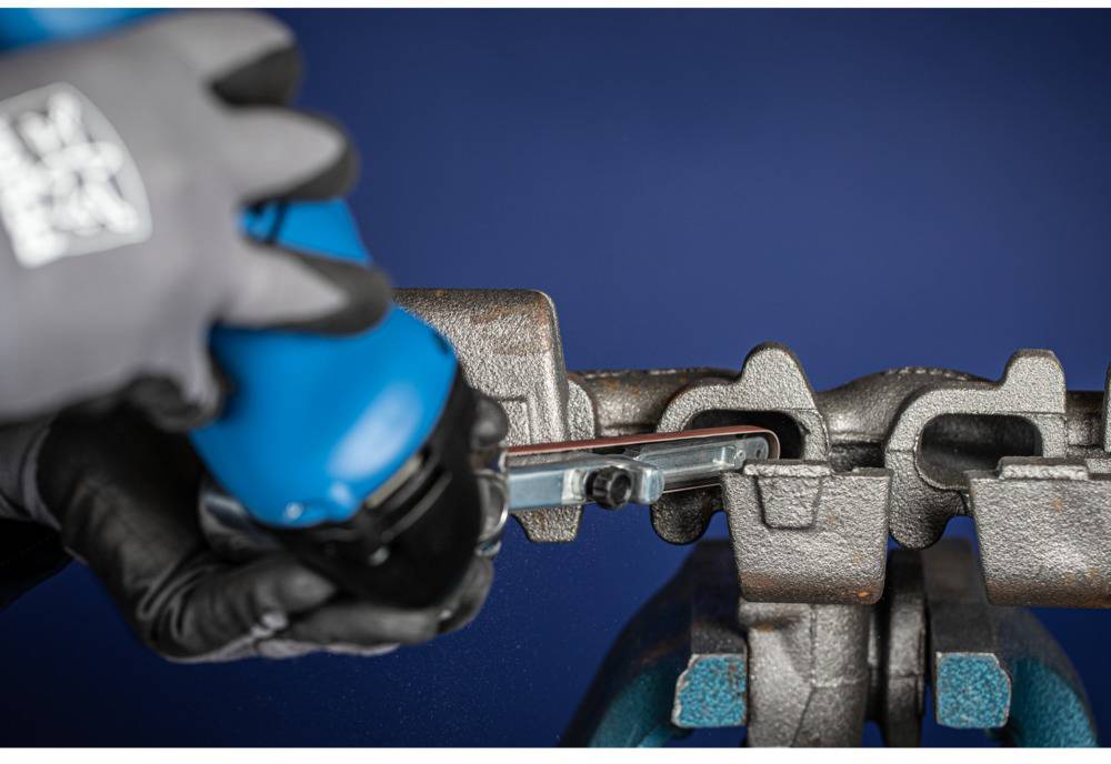 'A close-up of hands wearing protective gloves positioning a blue tool against a metallic component. Dark blue background.'