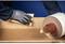 A person wearing gloves is sanding a wooden surface with sandpaper. Beside them is a roll of sandpaper.