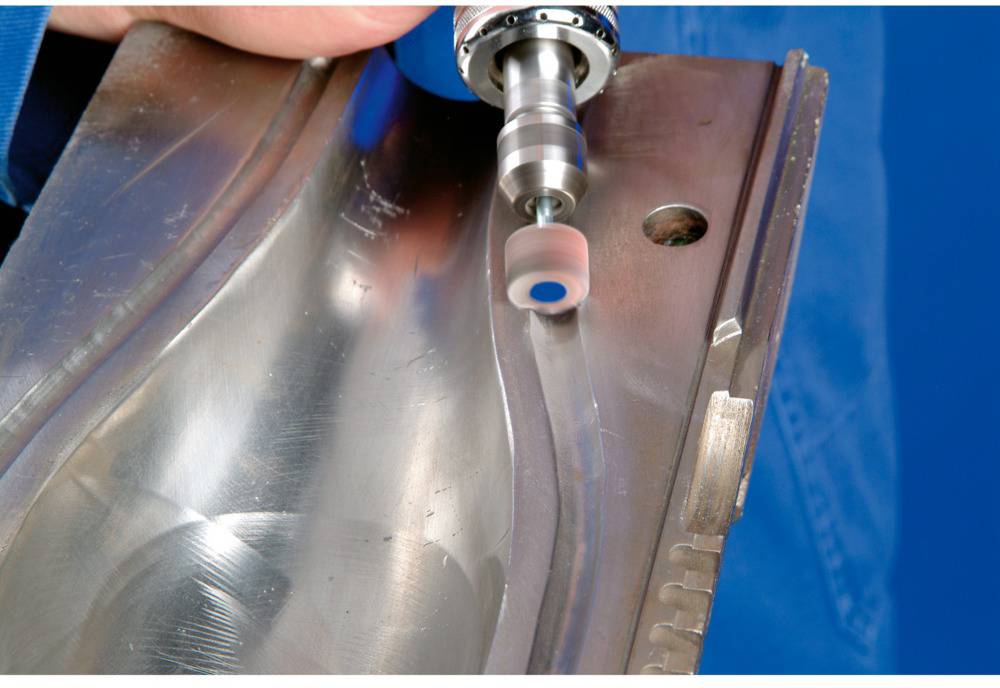 A hand holds a tool with a rotating grinding head, working a metal surface to create smooth edges.
