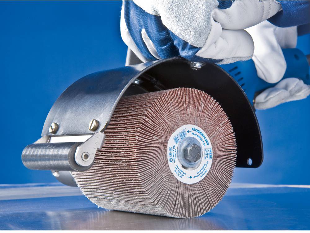 A person is holding a polishing machine with a grinding roller, which is being guided over a metal surface; focus on the tool and movement.