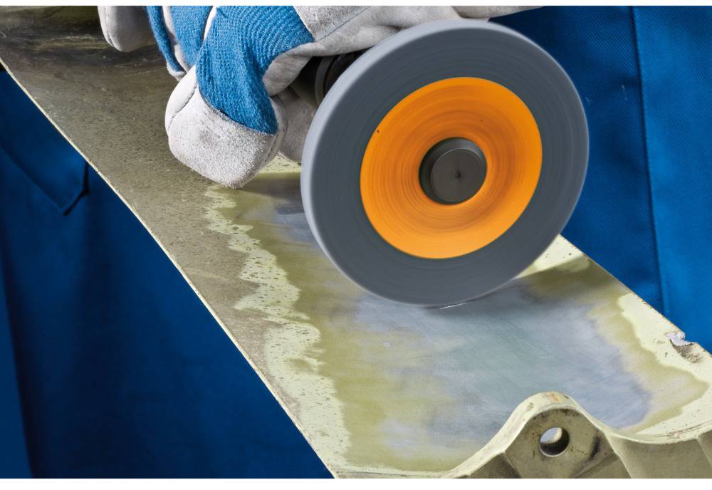 Hand holding a grinding wheel, polishing a metal surface. Protective glove and blue cloth visible. Grinding process in progress.