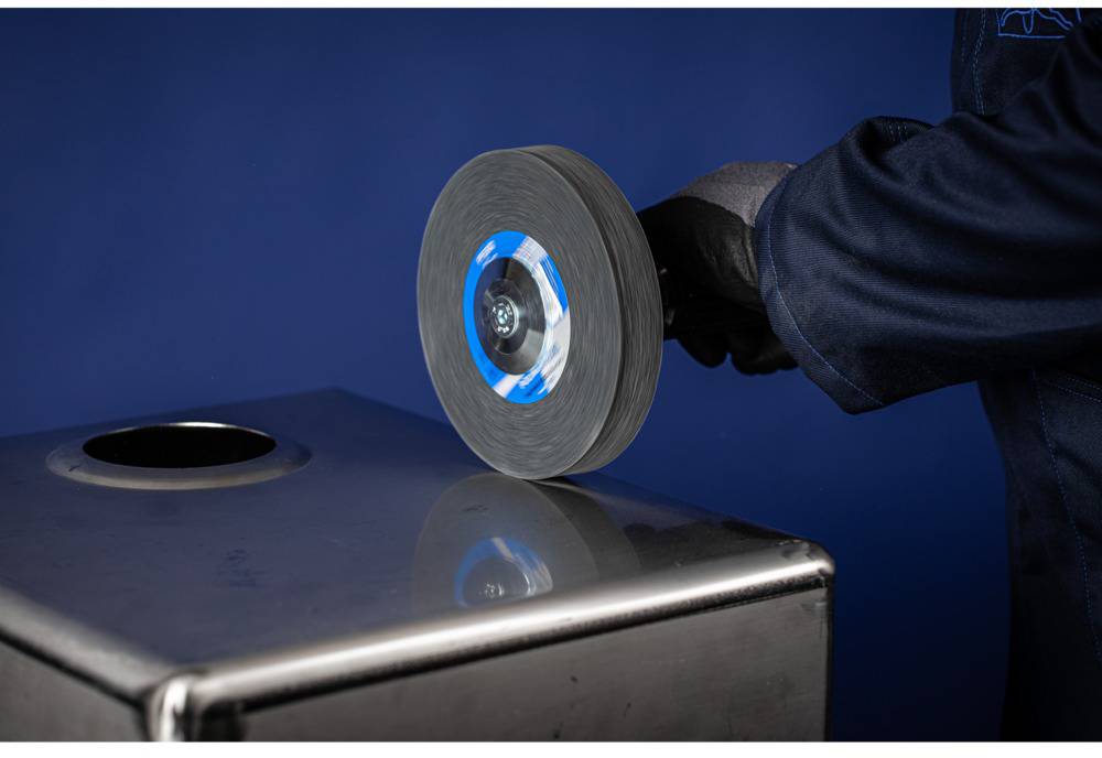 A hand in a glove holds a grinding tool over a metal container. The background is blue.