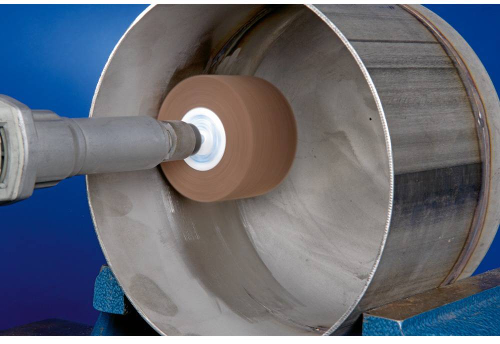 A machine is grinding the interior of a large metal pipe. A grinding head rotates inside the pipe to smooth the surface.