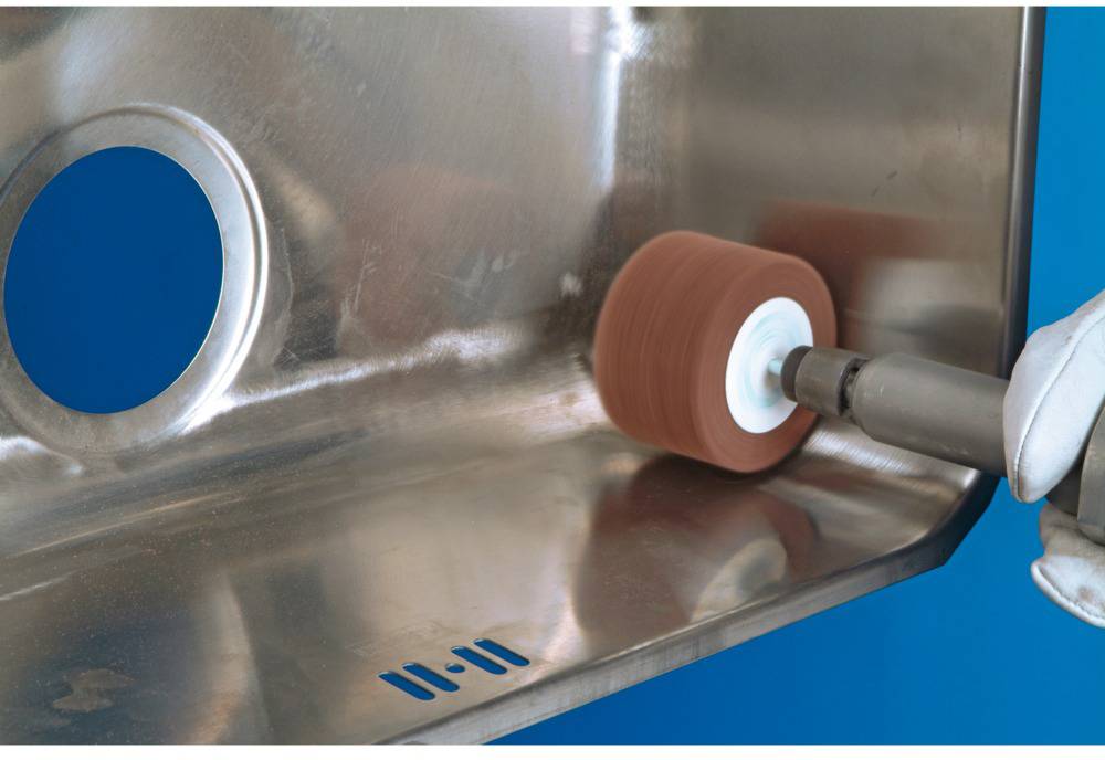 A stainless steel sink is hand-polished to a high shine using a rotating polishing disc. One person is holding the tool.