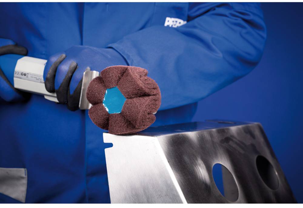 A person in blue workwear is processing a metal surface using a machine with a grinding attachment.