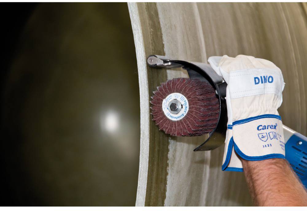 A person is grinding a curved metal surface with a machine while wearing gloves.