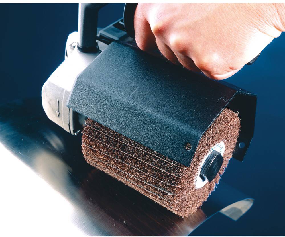 A hand holds an electric grinding machine with a rotating disc that is polishing a metal surface.