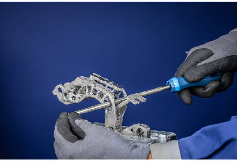 A person wearing gloves is filing a metal part. The background is dark blue.