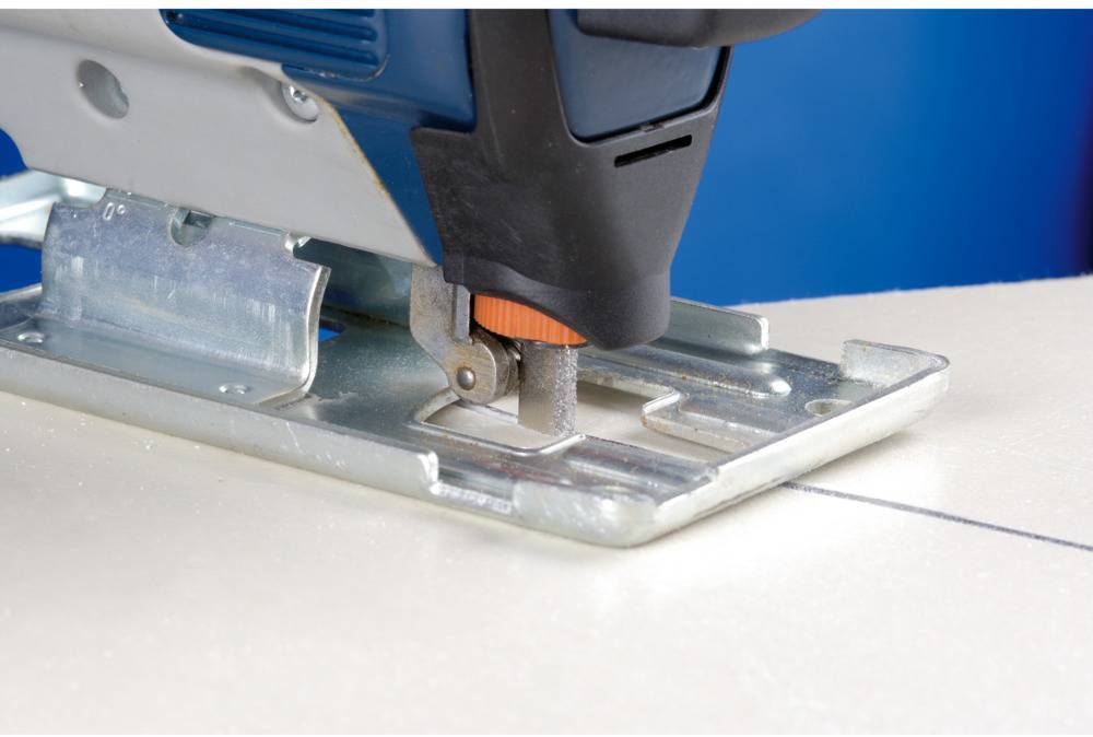 A jigsaw cuts along a straight line on a wooden board. The focus is on the blade and the saw blade.