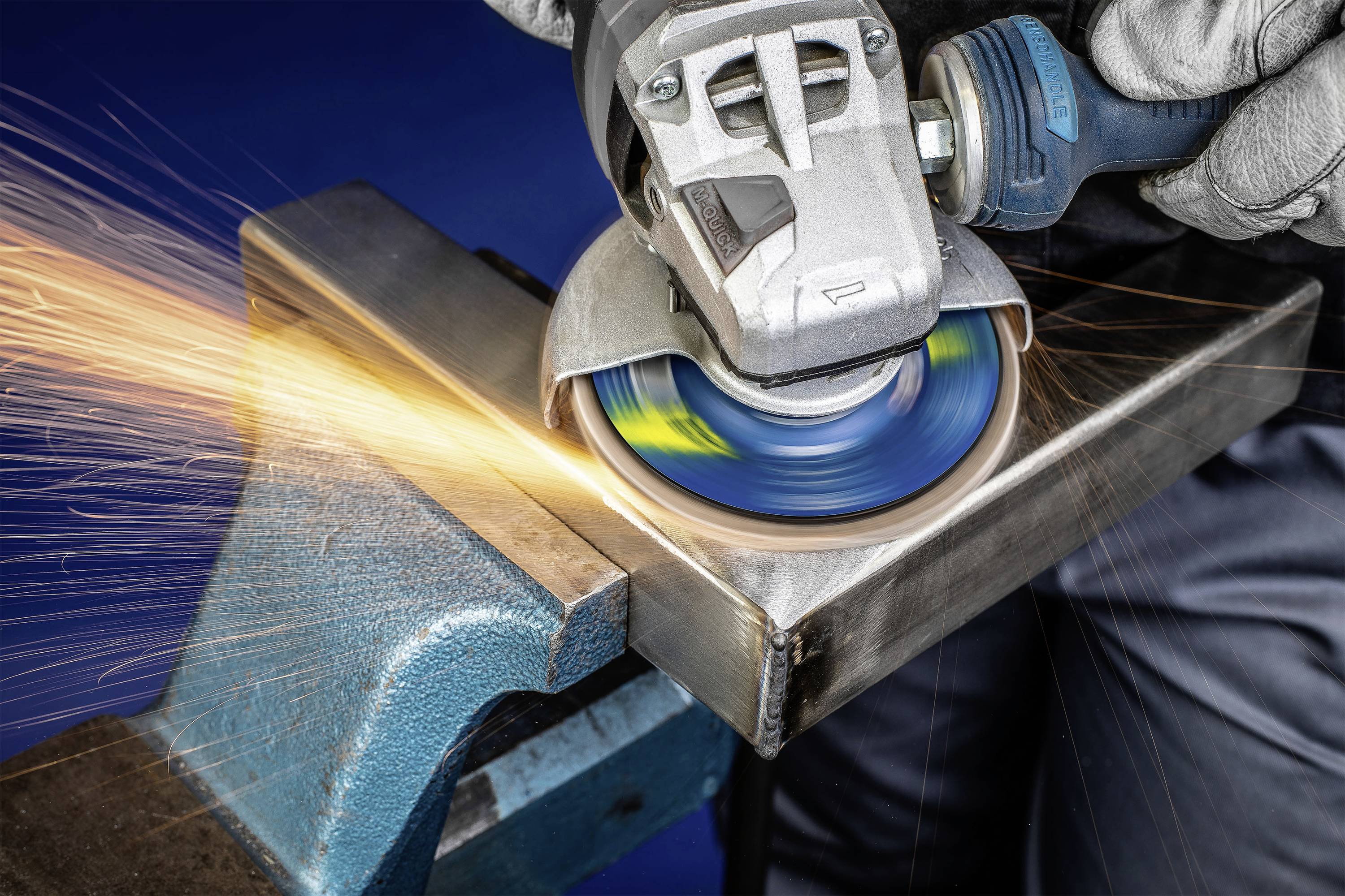 A person is grinding a metal piece with an angle grinder in a vice, with sparks flying to the side.