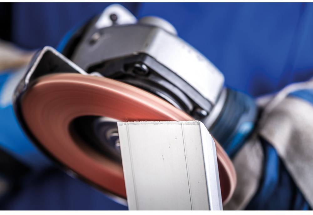 Close-up of a rotating grinding wheel machining metal. A worker in blue protective clothing is operating the machine.
