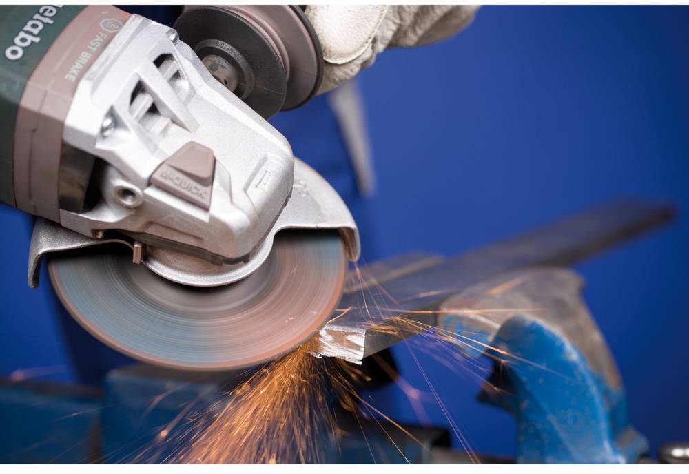 A person is grinding metal with an angle grinder, with sparks flying. The scene depicts skilled craftsmanship in a workshop.