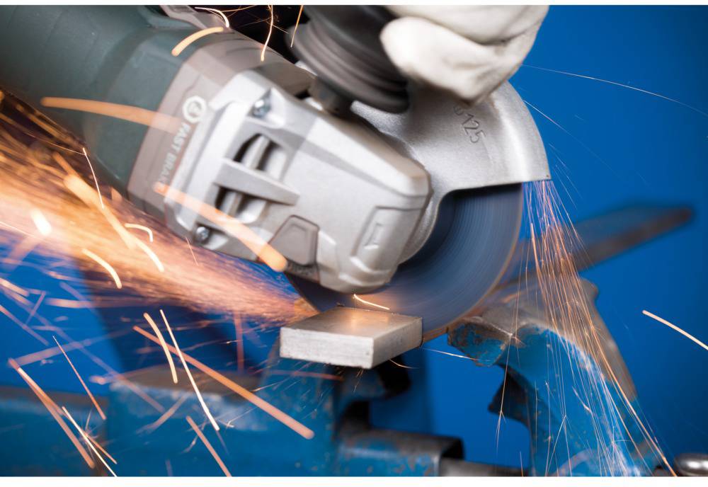 A hand is holding an angle grinder, which is spraying sparks while cutting a piece of metal clamped in a vice.