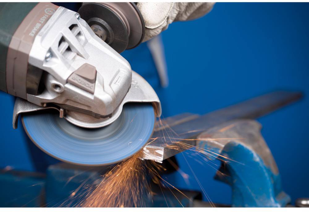 A hand is holding an angle grinder that is spraying sparks from a piece of metal against a blue background.