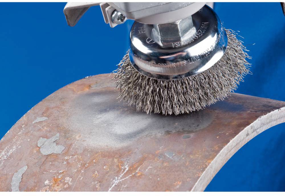 A wire brush polishes a rusty metal surface against a blue background.
