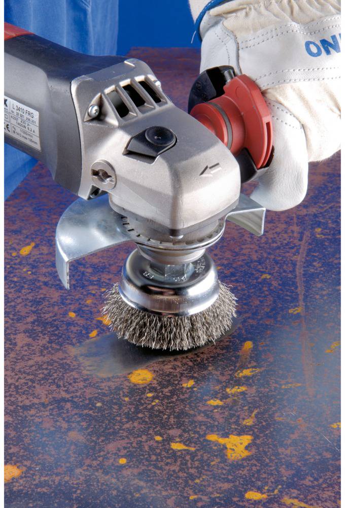 A person is using an electric wire brush with gloves to clean rusty metal.