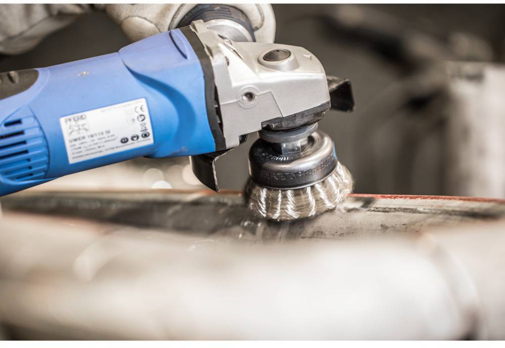 A close-up shows an electric grinding machine with a wire brush being used to polish or clean metal.