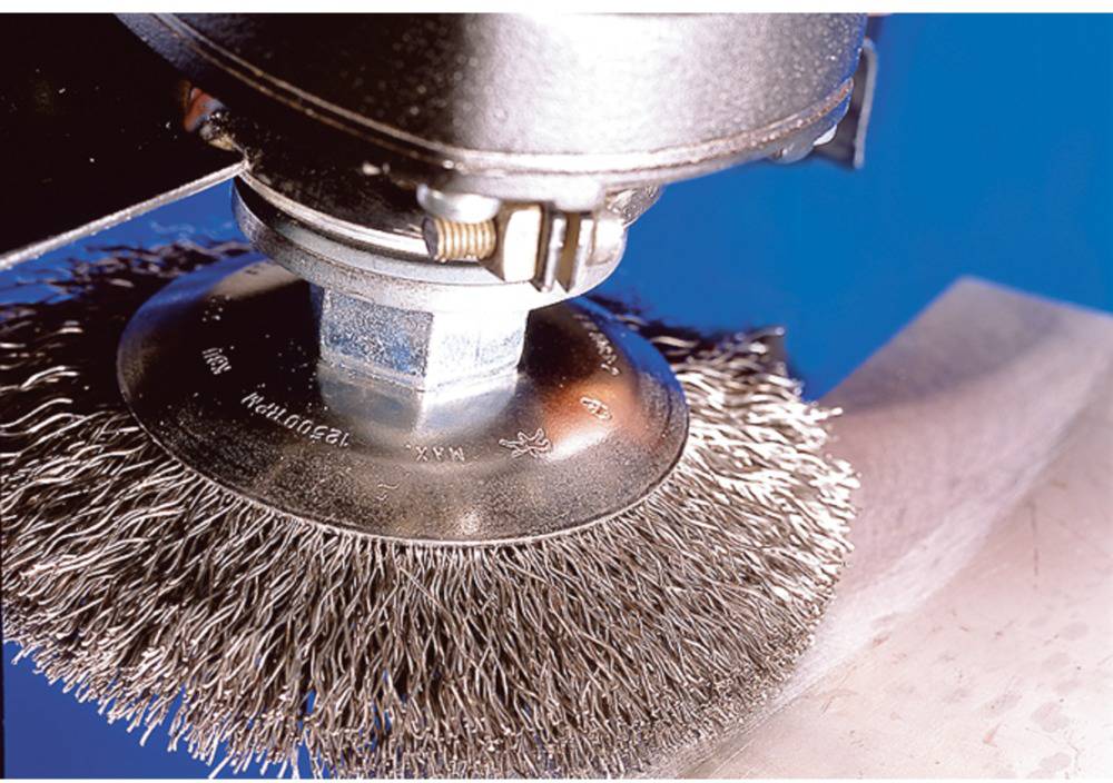 A rotating wire brush attachment is processing a metal surface to clean or polish it.