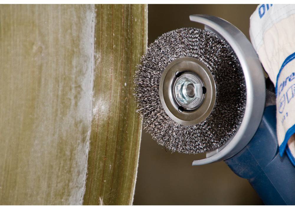 Close-up of an angle grinder with a wire brush, cleaning the surface of a metal. One hand is holding the tool steady.