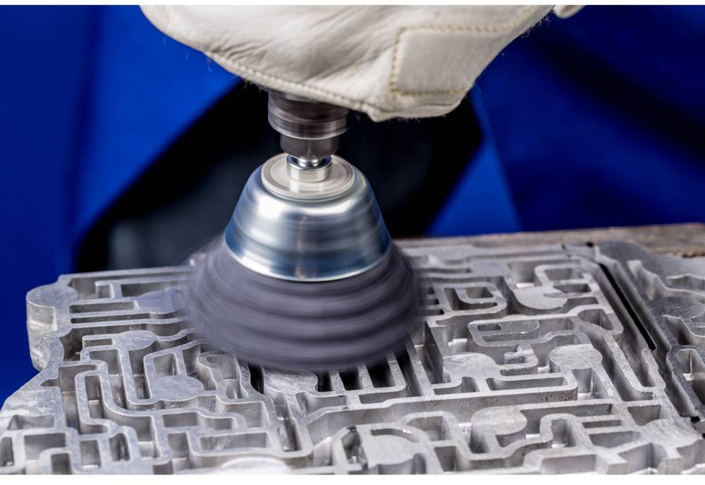 A person is polishing a complex-shaped metal surface with a rotating tool to make the structure smooth and shiny.