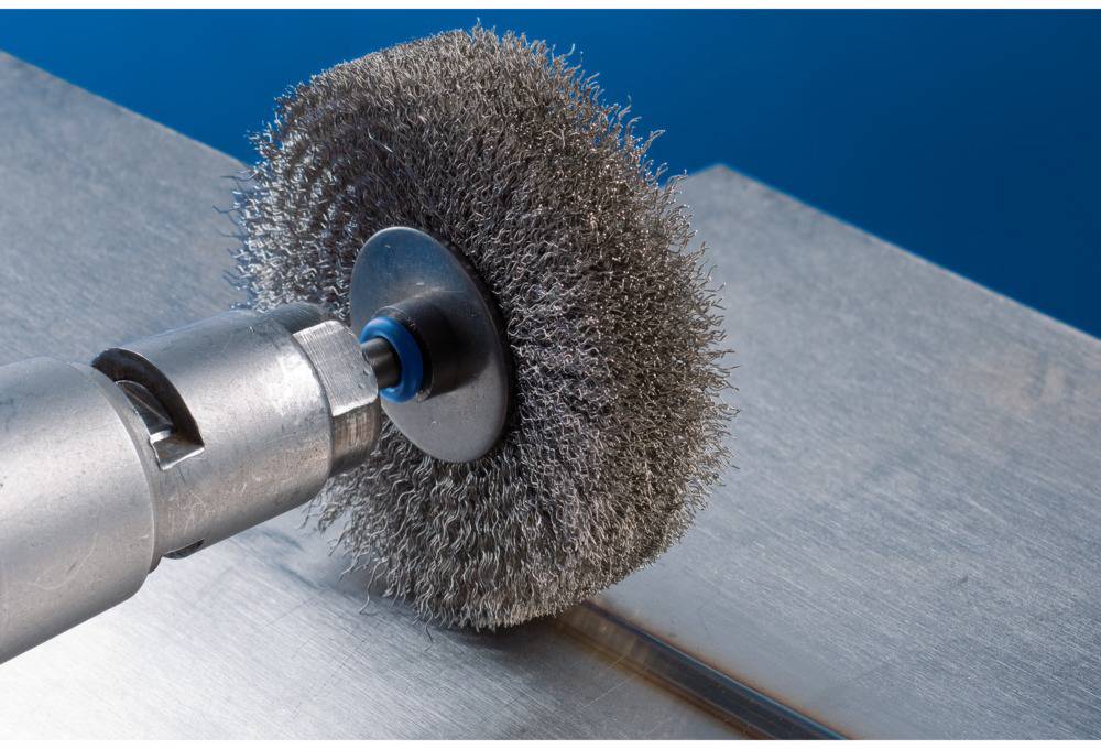 A wire brush polishes a metal surface. The brush rotates to clean and smooth the surface.