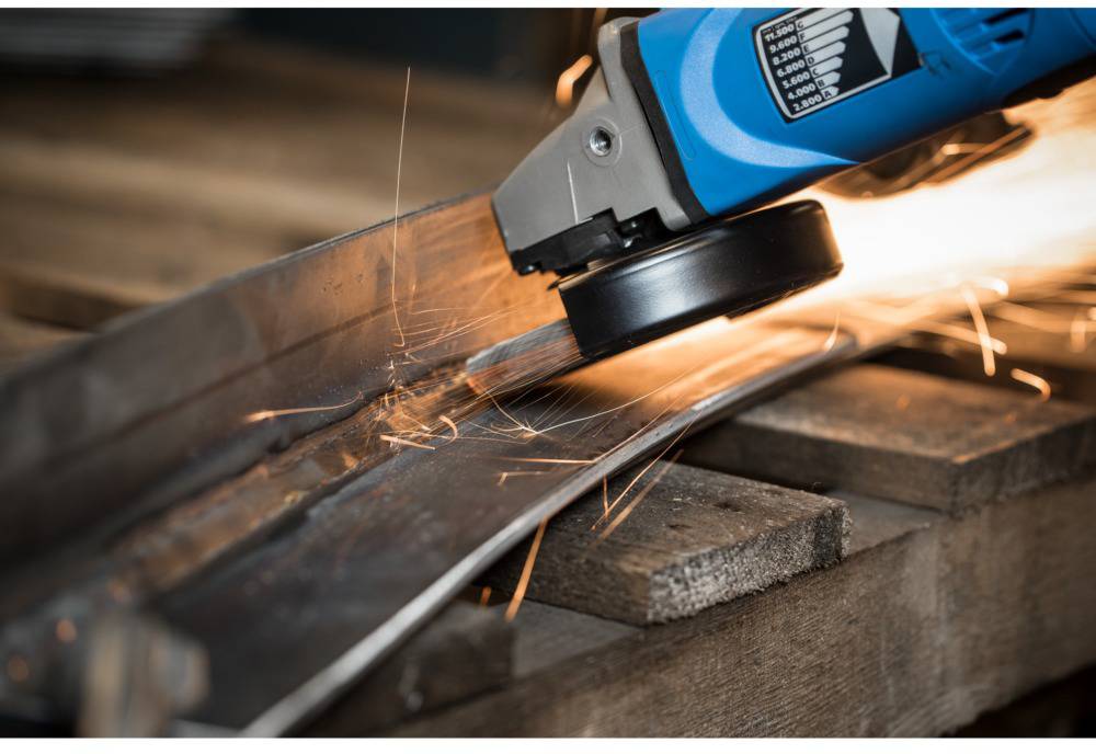 A close-up of a blue angle grinder spraying sparks as it grinds metal on a wooden surface.