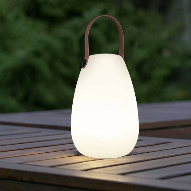 A portable, glowing lantern sits on a wooden table outdoors. It has a curved shape and a handle.