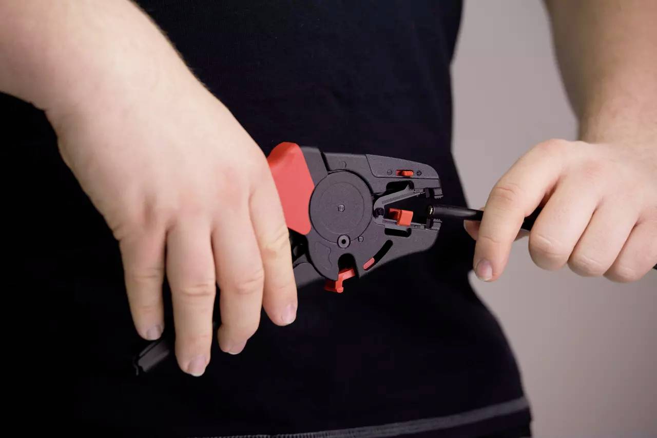 A person is holding a cutting tool and working on a cable. Hands are in focus, with the body remaining in the background.
