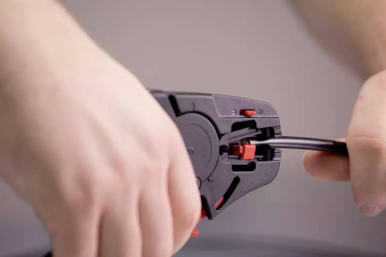 Hands are tightening the end of a black cable with a tool.