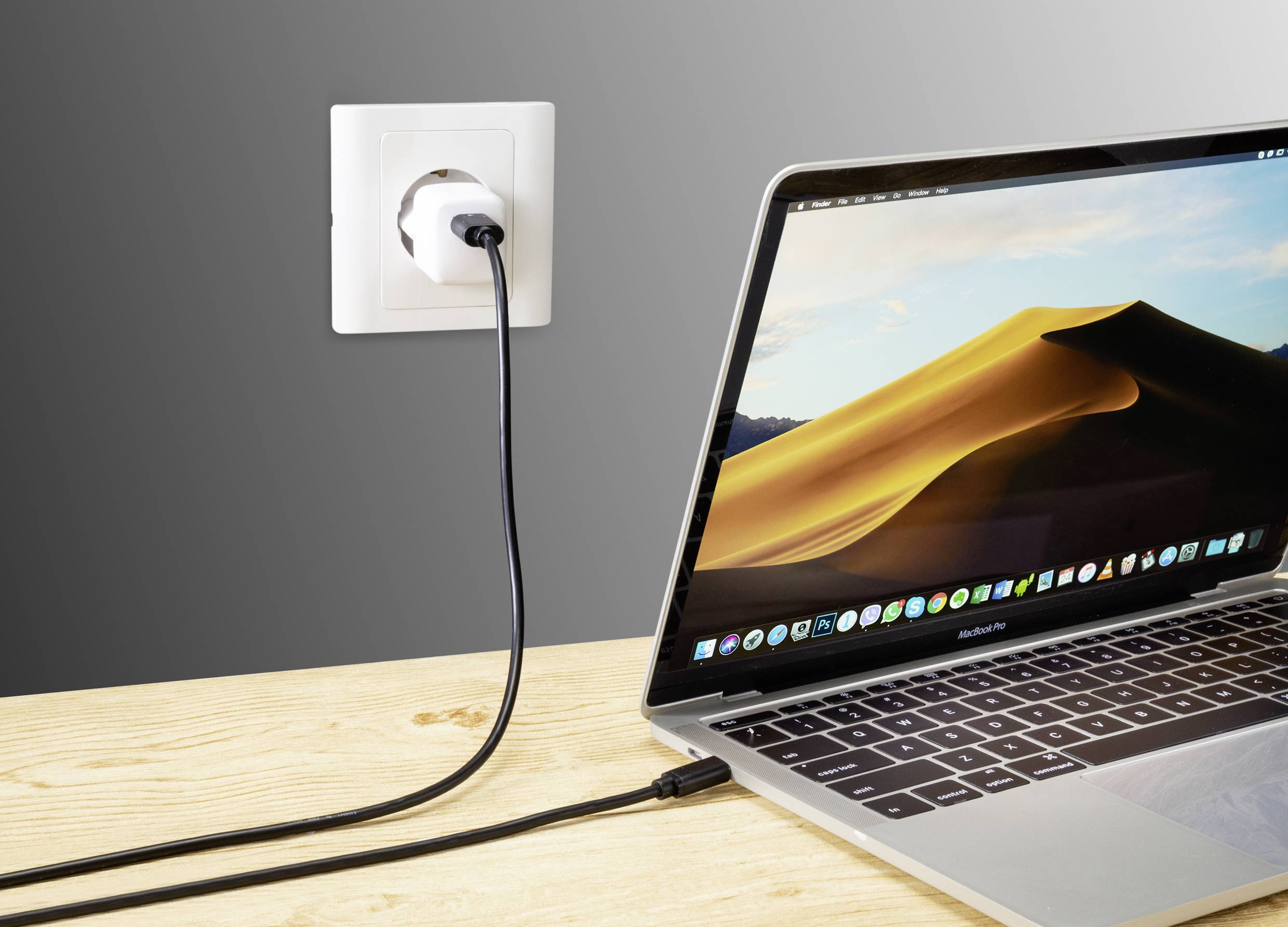 A laptop is connected to a plug socket with a charging cable. The screen displays a desert landscape.