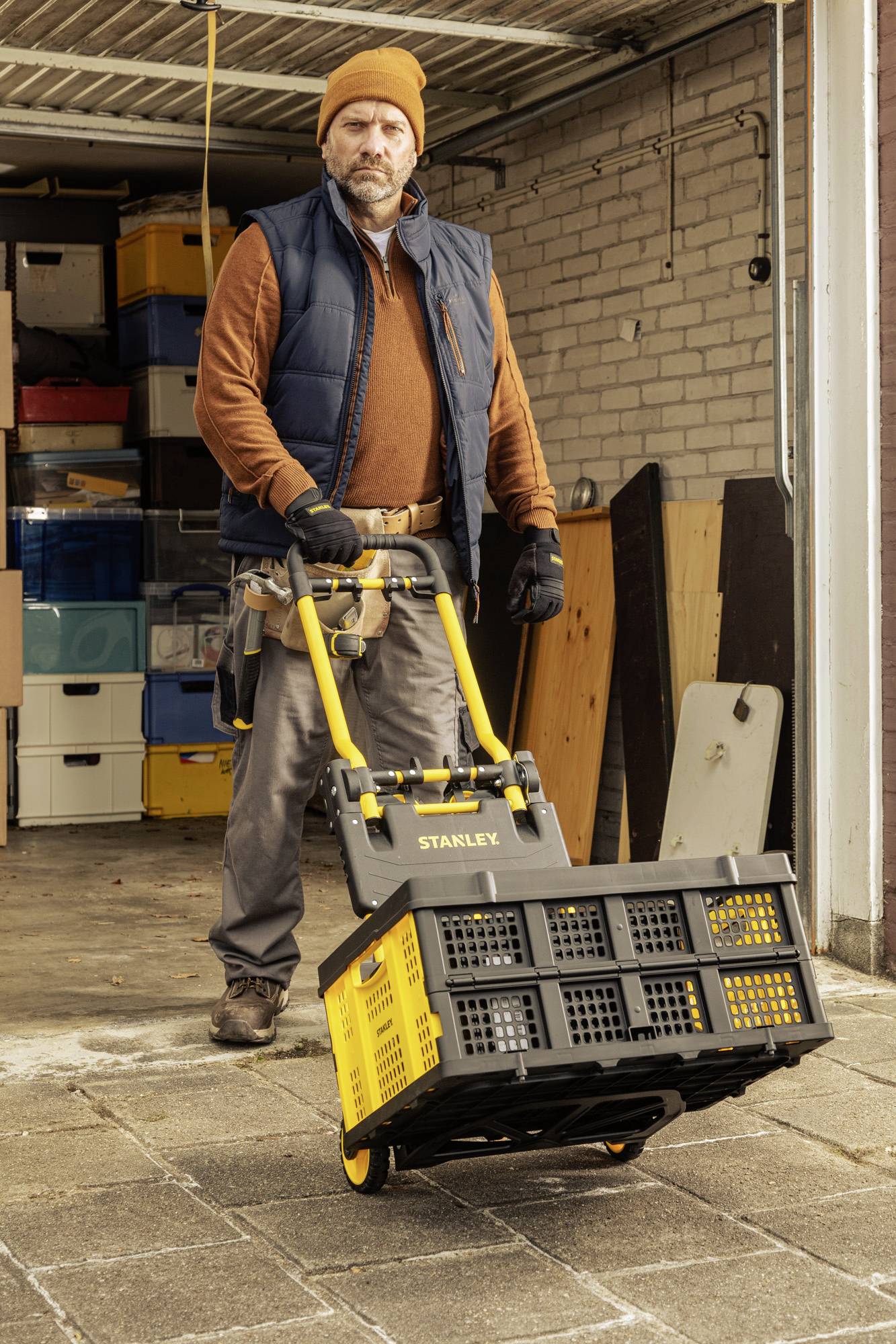 A man in a garage is pushing a yellow trolley laden with boxes. In the background, more boxes and shelves are visible.