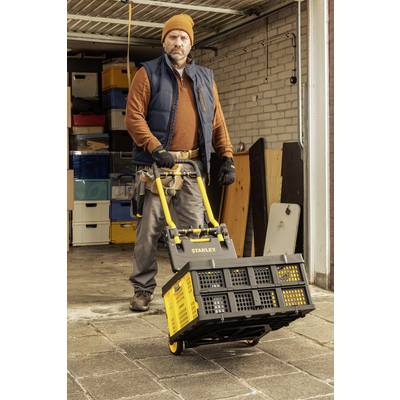 A man in a garage is pushing a yellow trolley laden with boxes. In the background, more boxes and shelves are visible.