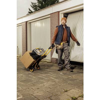 A man in work attire stands in front of an open garage door, holding a sack barrow with a cardboard box and toolbox.