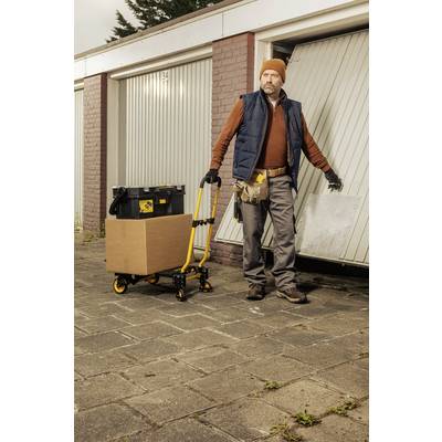 A man opens a garage door and holds a platform with a cardboard box and toolbox. He is wearing work clothes and a cap.