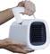 A person is holding a portable, white air cooler with a handle on top. The cooler is facing forward, with ventilation slots visible.