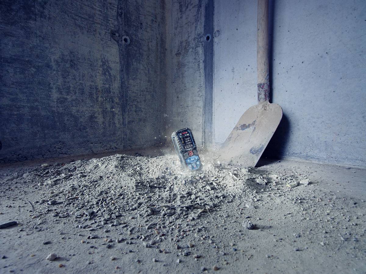 A mobile phone lies half-embedded in a dusty concrete surface next to a trowel in a grey corner of the room.