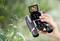 A hand holds a pair of binoculars with an integrated screen, displaying an image of an animal, surrounded by nature.