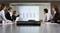 A group of business people are sitting in a conference room, looking at a presentation with a bar chart on a screen.