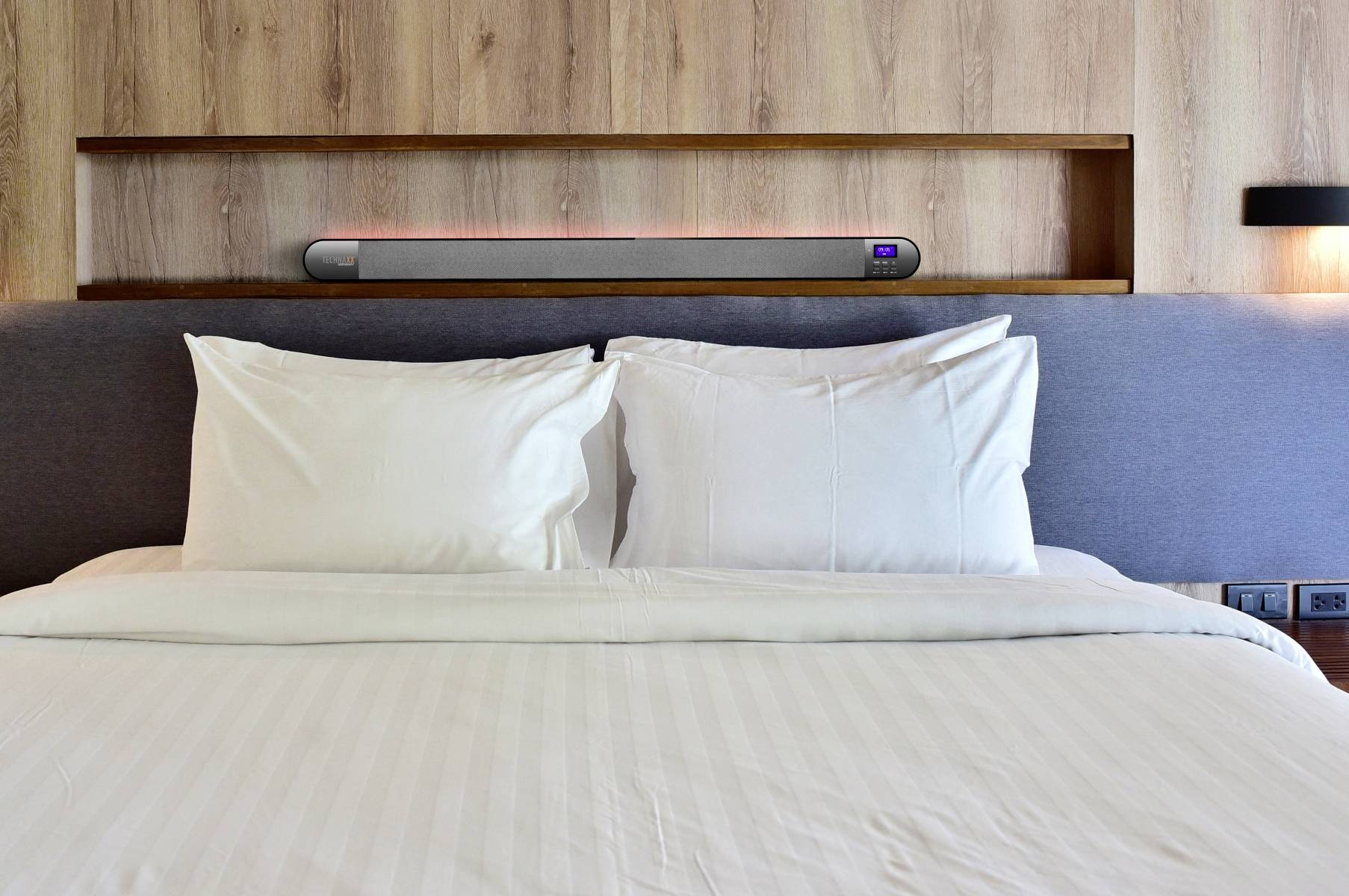 A modern, neatly made bed with white pillows and bedding in front of a wood-panelled wall in the bedroom.