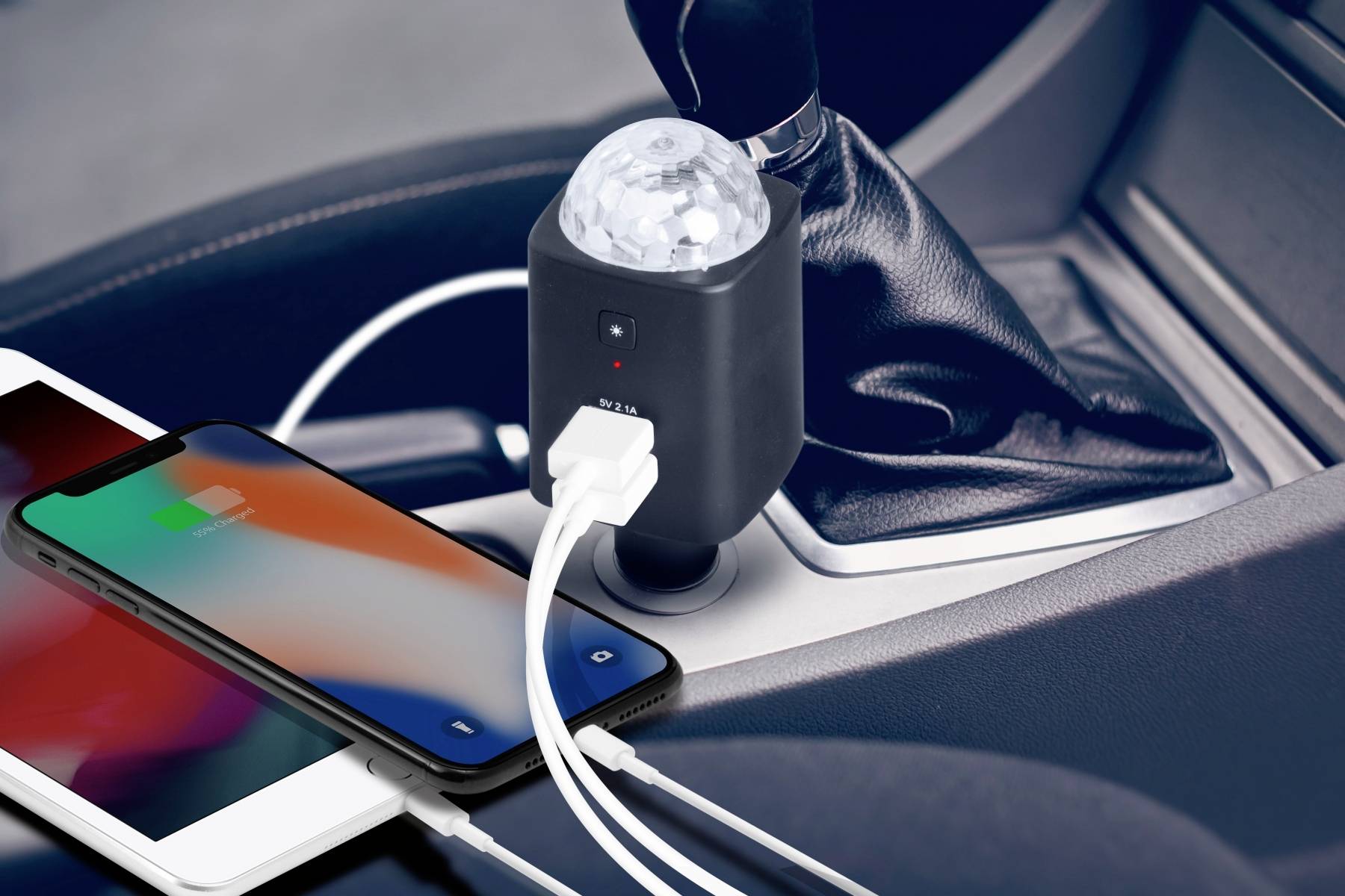 'Two smartphones charging via USB through a charger in the car, plugged into the cigarette lighter next to the gear stick.'