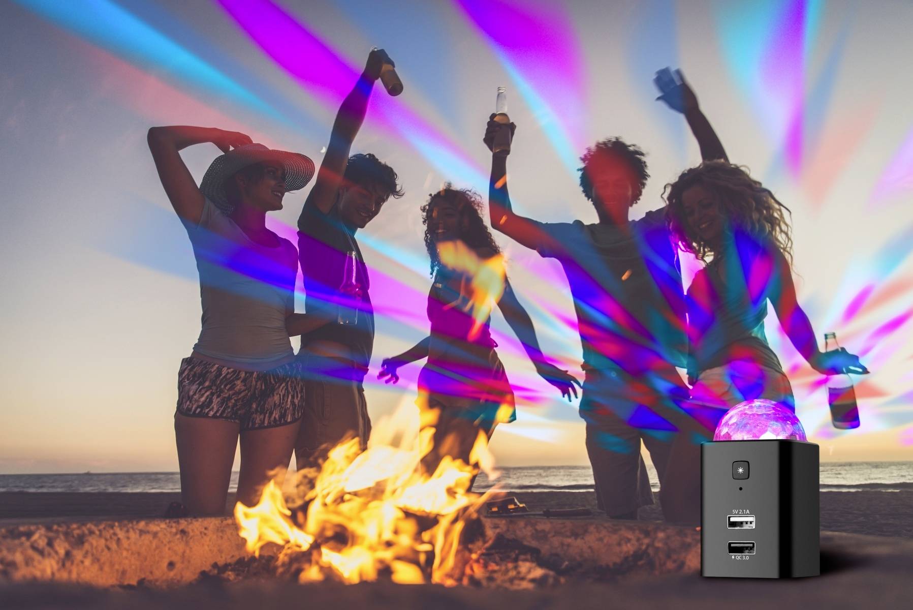 A group of people dance joyfully around a campfire on the beach at sunset. Colourful lights illuminate the scene.