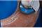An angle grinder is working on a rusty steel pipe. The grinding disc is in operation, smoothing the material.