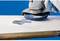 A sanding machine smooths the surface of a white board. A worker holds the device, which generates dust particles, against the surface.