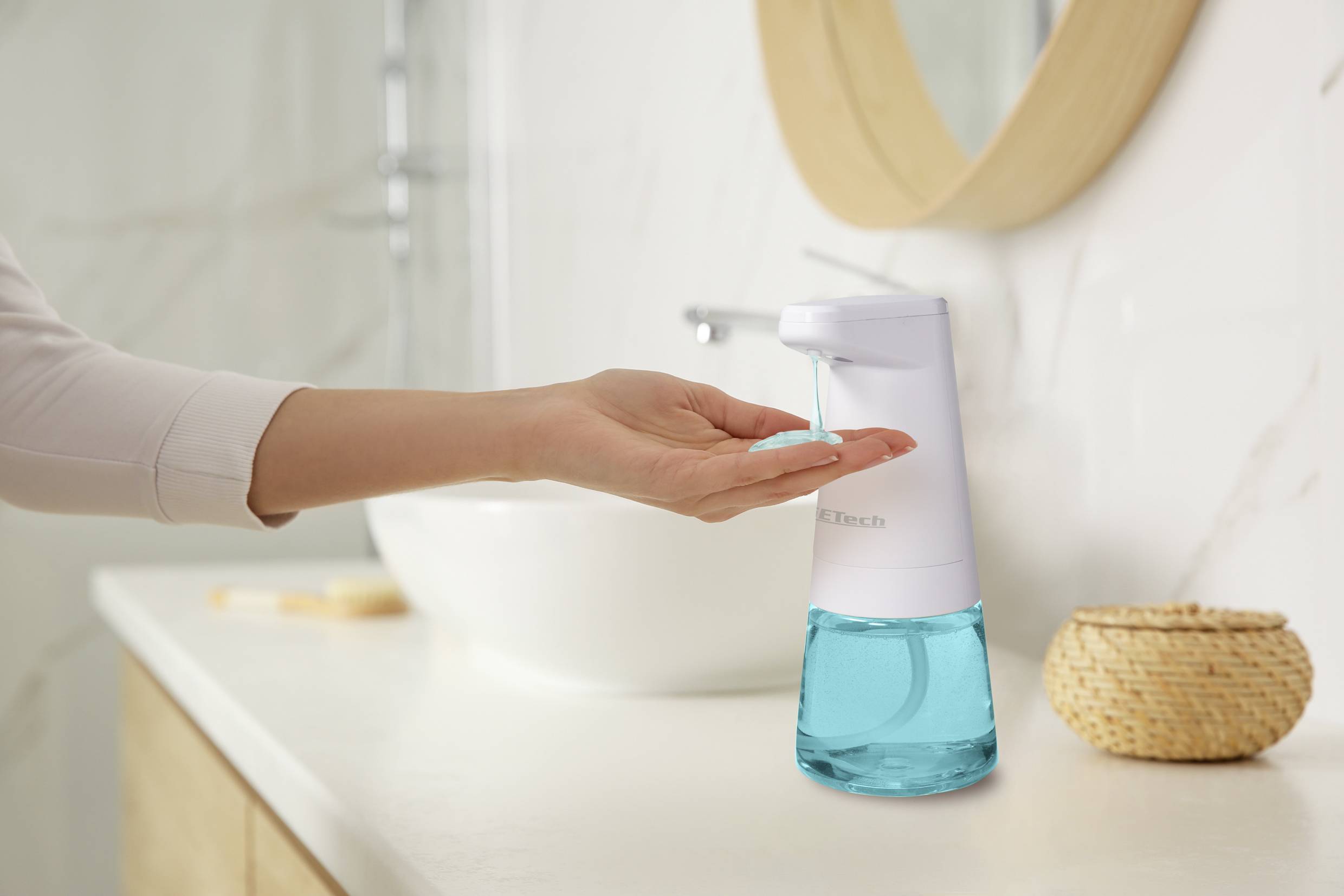 A hand is held beneath an automatic soap dispenser in the bathroom, ready to dispense soap.